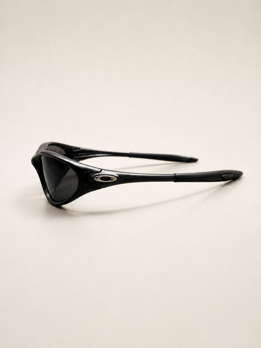 Rear three-quarter view of black Oakley Minute sunglasses, showing open temple arms and silver oval side details.